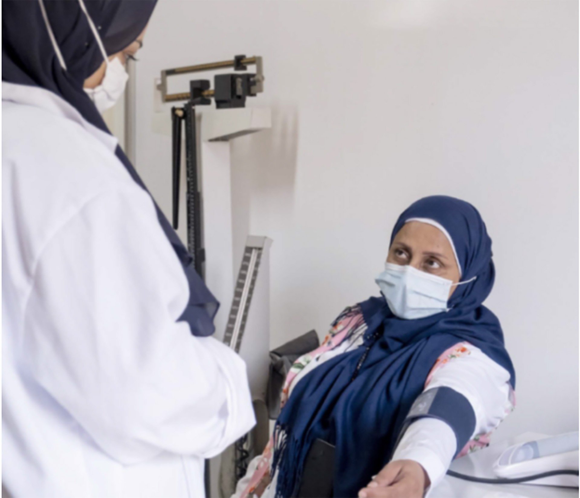 two people wearing masks and a headscarfs taking blood pressure